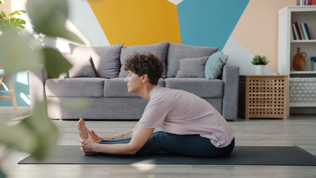 Woman stretching on yoga mat in living room.
home yoga practice Start yoga practice home simple beginning grounding Blue Osa method