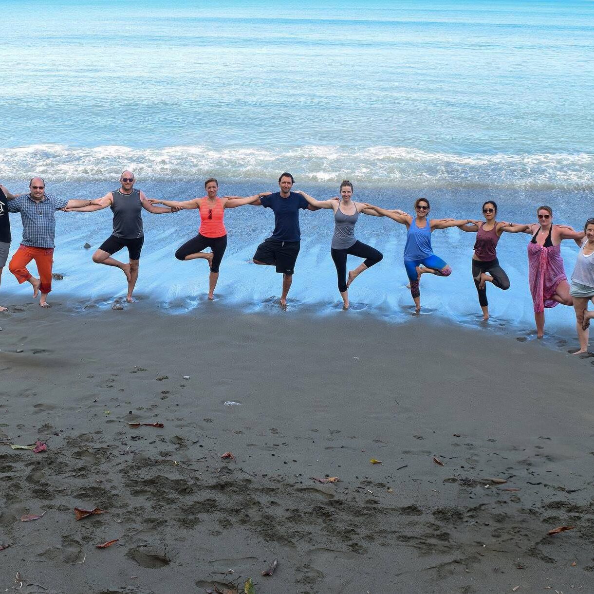 Group of yogis doing tree pose on the beach together facing the ocean during Blue Osa Yoga Retreat & Spa's Costa Rica Yoga Teacher Training Program